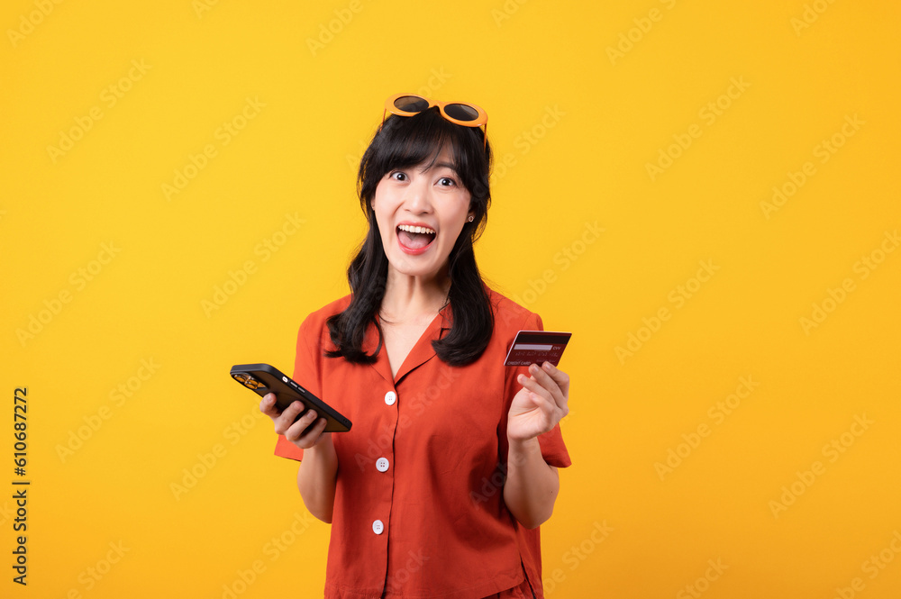 Portrait young beautiful asian woman happy smile dressed in orange clothes using credit card purchase shopping online on smartphone isolated on yellow background. Pay and purchase payment concept. Portrait young beautiful asian woman happy smile dressed in orange clothes using credit card purchase shopping online on smartphone isolated on yellow background. Pay and purchase payment concept.