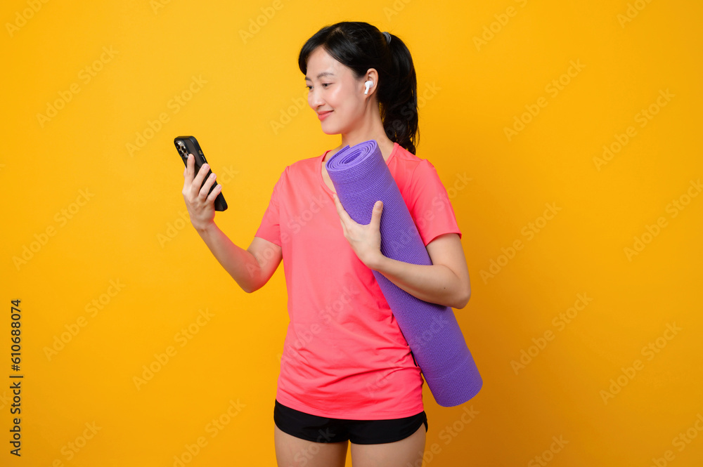 Portrait young asian sports fitness woman happy smile wearing pink sportswear and smartphone doing exercise training workout against yellow studio background. technology wellness lifestyle concept. Portrait young asian sports fitness woman happy smile wearing pink sportswear and smartphone doing exercise training workout against yellow studio background. technology wellness lifestyle concept.