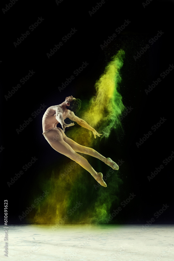 Obraz premium Muscular young man, professional ballet dancer in motion, dancing with colorful powder explosion against black studio background. Concept of art, festival, beauty of dance, inspiration, youth