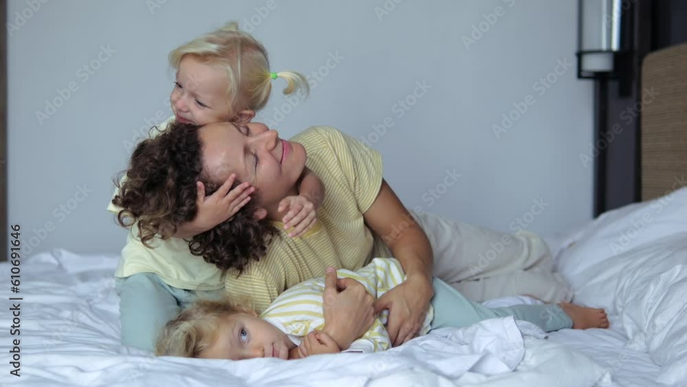 Loving happy kids hug their beloved mother lying resting on bed together. Children love and hug their mother tightly. Concept of happy motherhood parenting with cute loving children, daughters. Loving happy kids hug their beloved mother lying resting on bed together. Children love and hug their mother tightly. Concept of happy motherhood parenting with cute loving children, daughters.