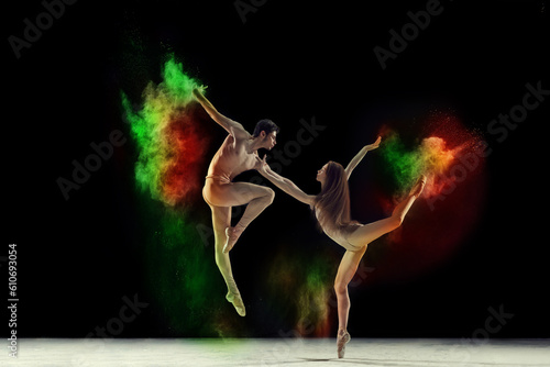Beautiful young man and woman, talented ballet dancers in beige bodysuits dancing with colorful powder explosion against black background. Concept of art, festival, beauty of dance, inspiration, youth