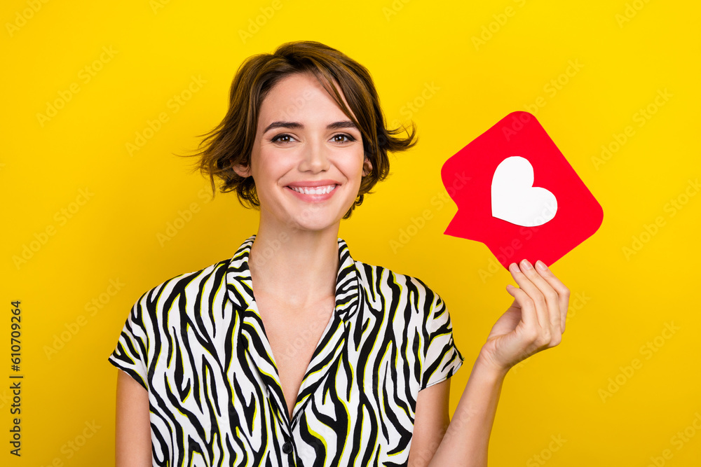 Photo of cute lady hold heart shape social media paper like icon watch post wear print shirt isolated yellow color background Photo of cute lady hold heart shape social media paper like icon watch post wear print shirt isolated yellow color background