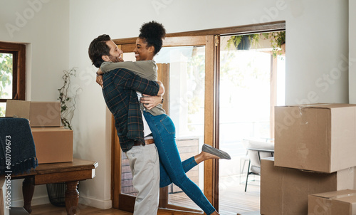 Happy interracial couple hug in new home for property relocation, renovation or investment together. Excited man embrace woman in real estate, house and boxes for moving, mortgage loan or celebration