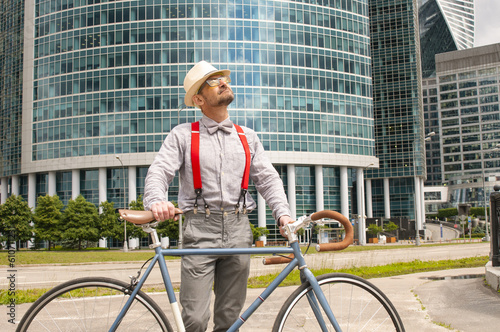 Adult hipster man with retro fixed gear bicycle on modern skyscrapers background
