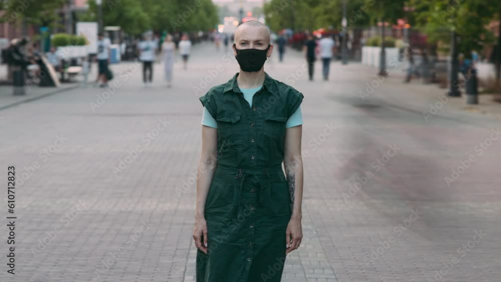 Zoom-in time lapse portrait of serious woman in medical mask standing outside in city during covid-19 pandemic. People walking fast in busy street. Zoom-in time lapse portrait of serious woman in medical mask standing outside in city during covid-19 pandemic. People walking fast in busy street.