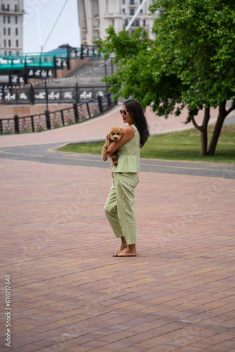 A beautiful Asian girl (Kazakh) holds a dog (mini poodle) in her hands. Summer portrait of a young woman in the park. © Татьяна Оракова