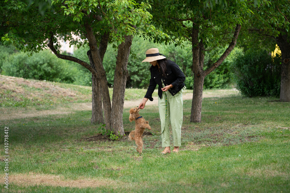 An Asian girl (Kazakh woman) feeds her dog (mini poodle) from her hands. Summer portrait of a young woman in the park.