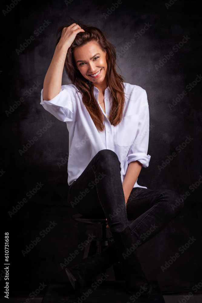 Studio portrait of a brunette haired mid aged woman sitting at isolated dark background Studio portrait of a brunette haired mid aged woman sitting at isolated dark background