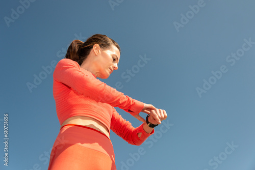 Female jogger checking her smart watch during exercise outside, blue sky background.