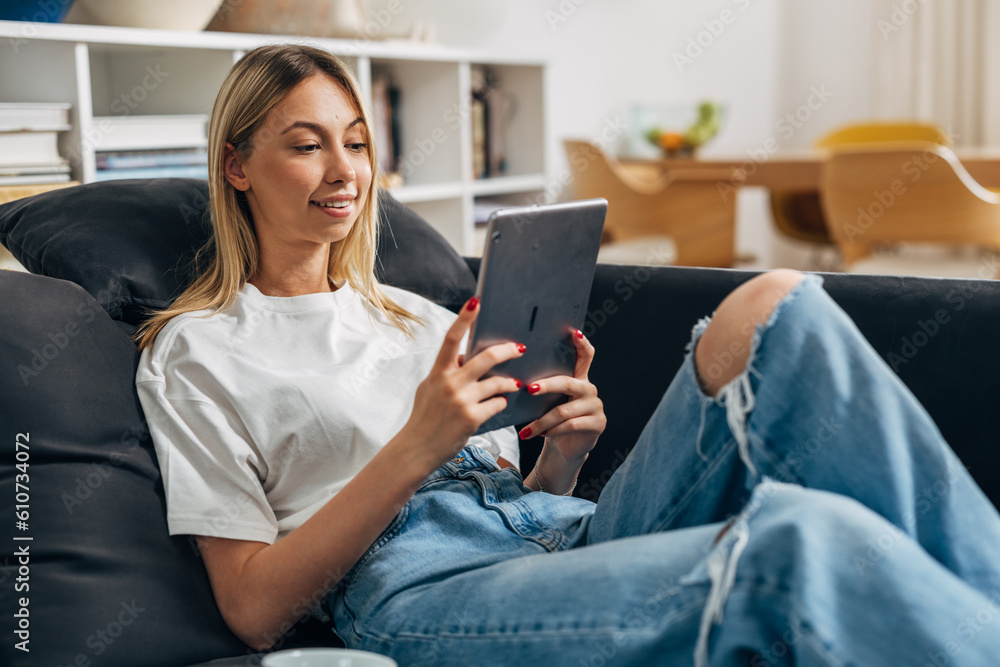 Young blond Caucasian woman is siting on the sofa and using digital tablet. Young blond Caucasian woman is siting on the sofa and using digital tablet.