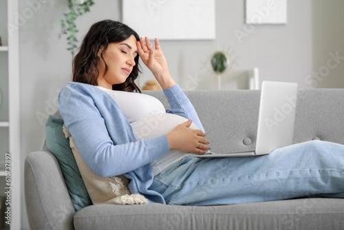 Tired young pregnant woman working with laptop on sofa at home