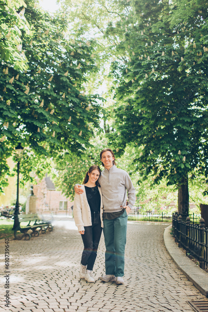 young couple walking down a tree lined street in a park holding hands and standing looking at the camera young couple walking down a tree lined street in a park holding hands and standing looking at the camera