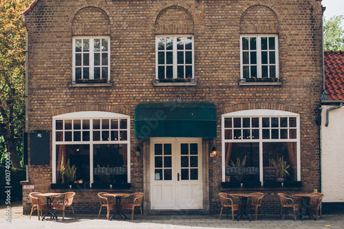 Photography front of an old brick building in europe with cafe tables in front and a green a