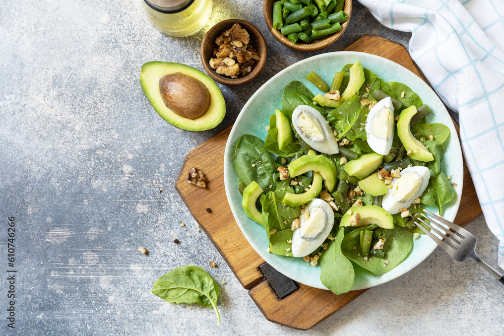 Organic green avocado and spinach salad with eggs, green beans, nuts on a stone table. Healthy food, summer healthy eating. View from above. Copy space. Organic green avocado and spinach salad with eggs, green beans, nuts on a stone table. Healthy food, summer healthy eating. View from above. Copy space.