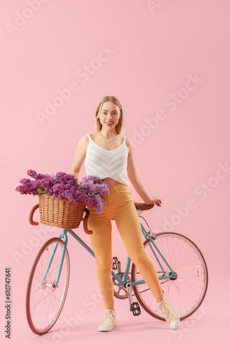 Fototapeta Naklejka Na Ścianę i Meble -  Young woman with lilac flowers and bicycle on pink background