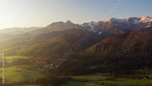 Mountains aerial drone shot snowy mountain peaks green hills covered with pine trees lit with orange sunrise light, epic mountain range, top view, spring season early morning landscape golden hour