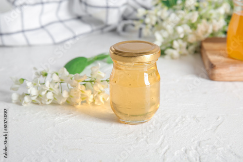 Jar of honey with flowers of acacia on light background, closeup