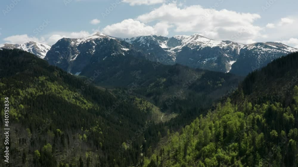 Top view mountain valley, high peaks covered with snow bright sun light, daylight, stunning aerial drone shot snowy mountains and green hills with pine trees, spring season mountain range landscape Top view mountain valley, high peaks covered with snow bright sun light, daylight, stunning aerial drone shot snowy mountains and green hills with pine trees, spring season mountain range landscape