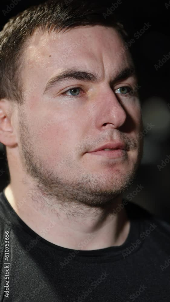 Vertical Screen: Bearded man bodybuilder with sweat on forehead wearing black t-shirt posing in dark gym, blurred lights on background. Closeup portrait of athlete after workout. Concept of sport Vertical Screen: Bearded man bodybuilder with sweat on forehead wearing black t-shirt posing in dark gym, blurred lights on background. Closeup portrait of athlete after workout. Concept of sport