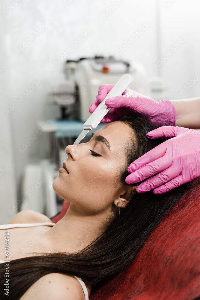 Fototapeta premium Ultrasonic facial and chin peeling for girl with ultrasonic scrubber in cosmetology clinic. Cleansing facial skin and removing blackheads with ultrasonic scrubber.