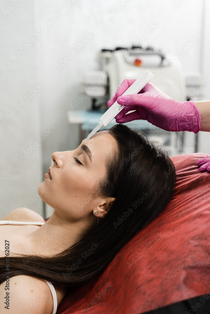 Naklejka premium Ultrasound facial peeling using scrubber close-up. Cosmetologist is doing ultrasonic peeling skin with skin scrubber for girl patient at cosmetology clinic.