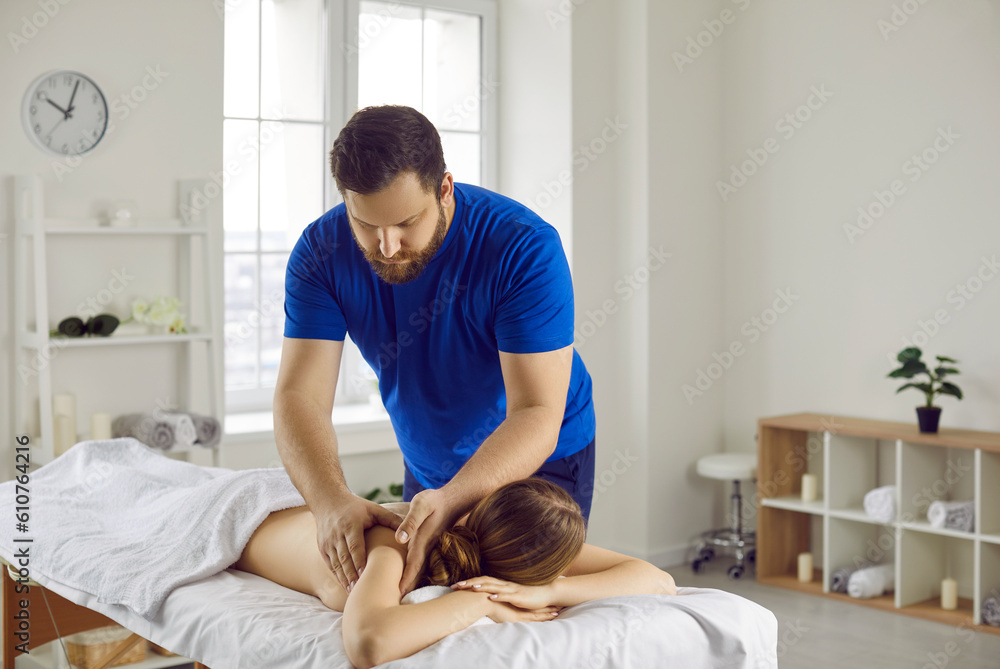 Young man in blue T-shirt, chiropractor or osteopath, massages back and shoulders of lying woman with hand movements during visit to manual therapy room. Professional chiropractor during work. Young man in blue T-shirt, chiropractor or osteopath, massages back and shoulders of lying woman with hand movements during visit to manual therapy room. Professional chiropractor during work.