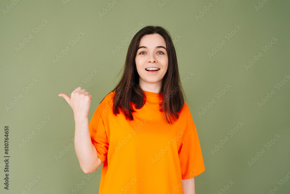 Cheerful lady in stylish orange clothing points to empty advertising space. Perfect for affordable promotions. Isolated on green background Cheerful lady in stylish orange clothing points to empty advertising space. Perfect for affordable promotions. Isolated on green background