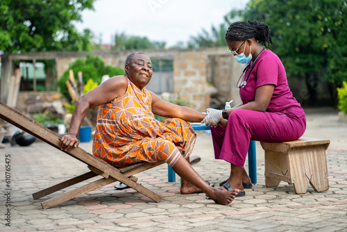 image of african aged woman receiving health care from home- young black nurse checking blood pressure from old woman outside