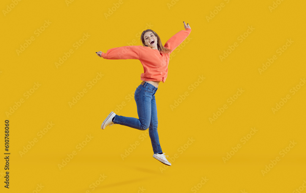Cheerful funny young woman jumps and stretches her arms isolated on bright yellow background. Happy woman in casual clothes jumps celebrating her success and victory. Concept of human emotions.