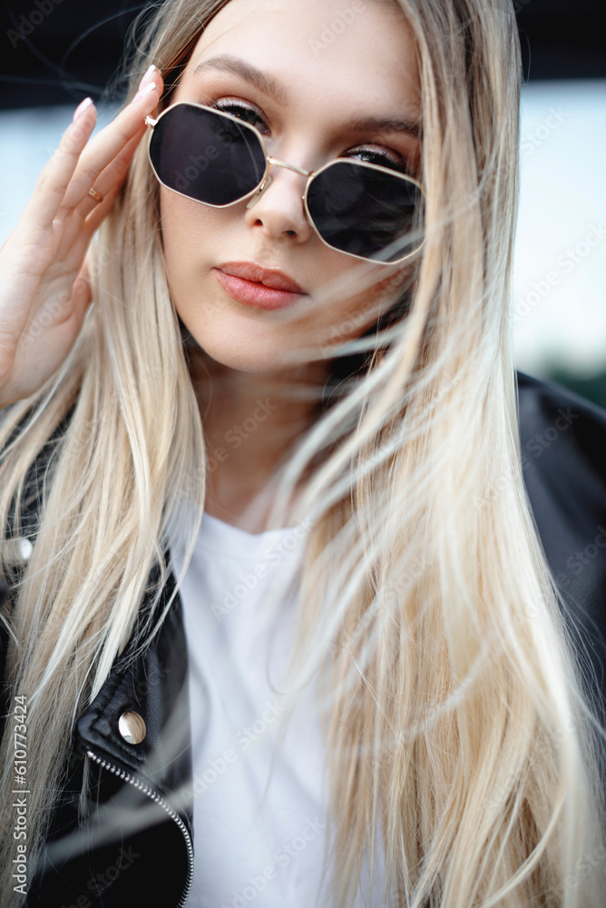 a beautiful girl in a leather jacket and black glasses near a shopping mall