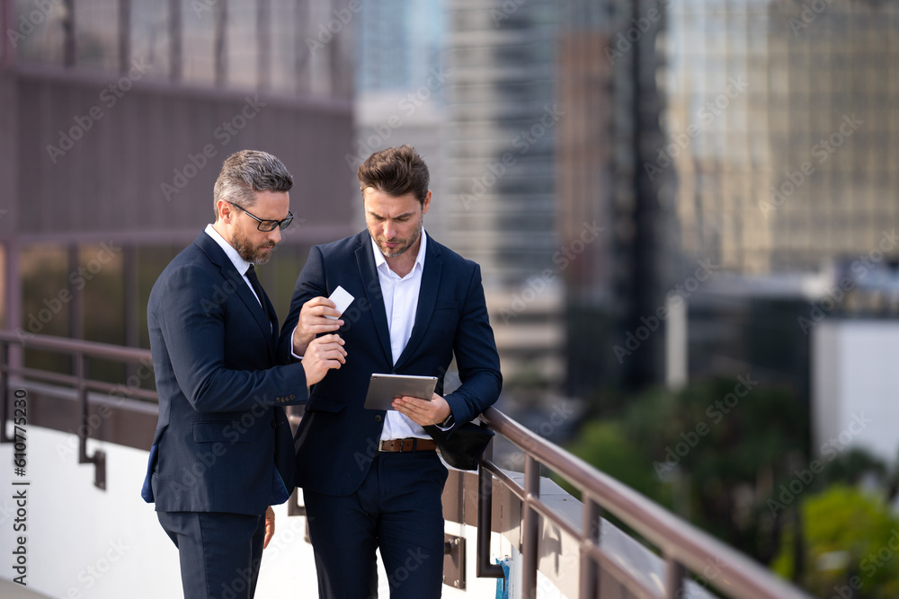 Online money transactions, mobile payments. Two business men in suit hold credit card and laptop tablet outdoor. Pay the bill. Man with credit card in city. Business deal of trading contract. Online money transactions, mobile payments. Two business men in suit hold credit card and laptop tablet outdoor. Pay the bill. Man with credit card in city. Business deal of trading contract.