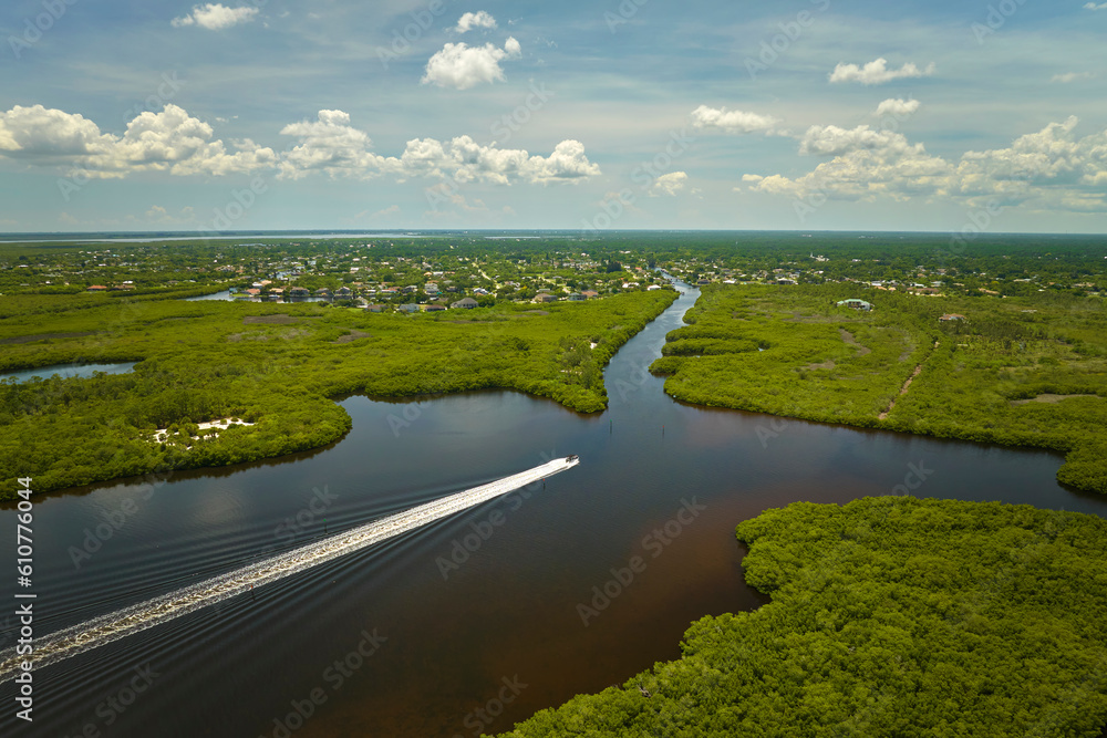 Aerial view of Florida wetlands with small motorboat swimming between green vegetation in water inlets. Recreation in nature concept