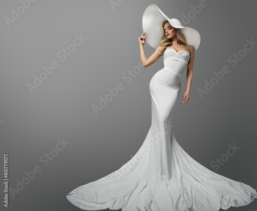 Fashion Woman in White Wedding Dress over Gray Background. Elegant Bride in Mermaid Gown and White Summer Hat. Beautiful Sexy Girl in Silk Long Dress