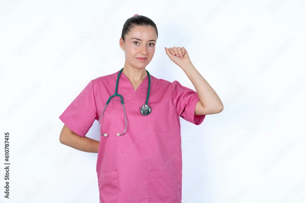 young caucasian doctor woman wearing pink uniform over white background feeling serious, strong and rebellious, raising fist up, protesting or fighting for revolution.