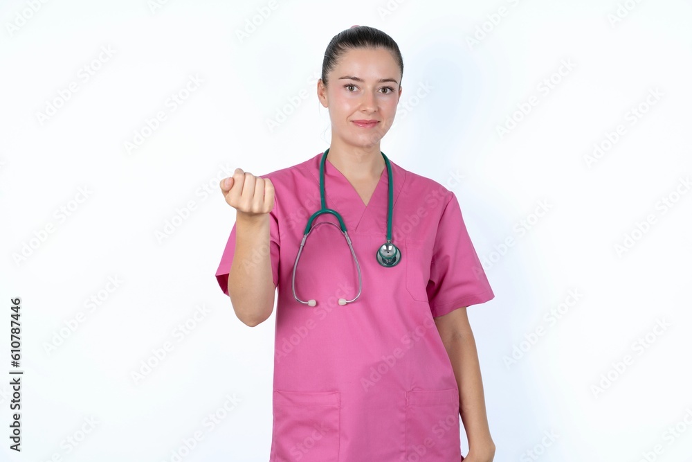 young caucasian doctor woman wearing pink uniform over white background , inviting you to come, confident and smiling making a gesture with hand, being positive and friendly. young caucasian doctor woman wearing pink uniform over white background , inviting you to come, confident and smiling making a gesture with hand, being positive and friendly.