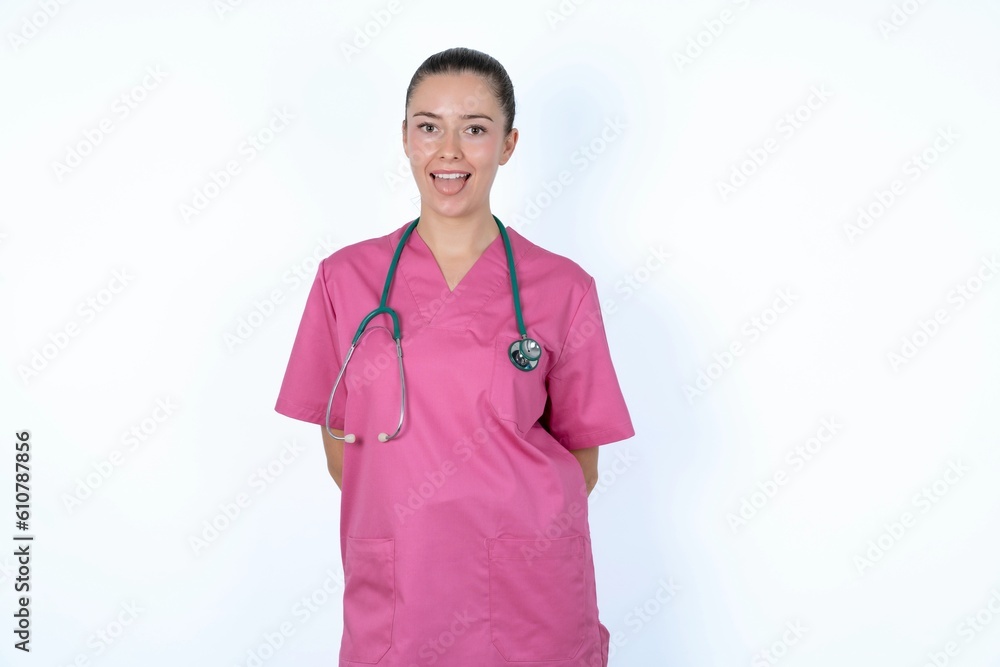 young caucasian doctor woman wearing pink uniform over white background with happy and funny face smiling and showing tongue. young caucasian doctor woman wearing pink uniform over white background with happy and funny face smiling and showing tongue.