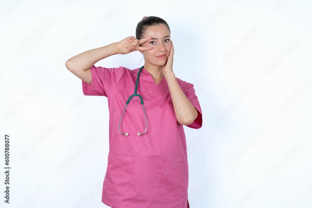 young caucasian doctor woman wearing pink uniform over white background making v-sign near eyes. Leisure lifestyle people person celebrate flirt coquettish concept.