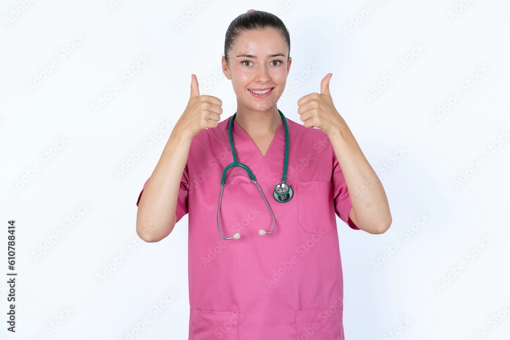 Optimistic young caucasian doctor woman wearing pink uniform over white background showing thumbs up with positive emotions. Quality and recommendation concept. Optimistic young caucasian doctor woman wearing pink uniform over white background showing thumbs up with positive emotions. Quality and recommendation concept.