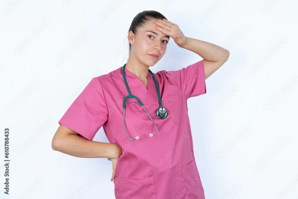 young caucasian doctor woman wearing pink uniform over white backgroundwiping forehead with hand making phew gesture, expressing relief feels happy that he prevented huge disaster. It was close enough young caucasian doctor woman wearing pink uniform over white backgroundwiping forehead with hand making phew gesture, expressing relief feels happy that he prevented huge disaster. It was close enough