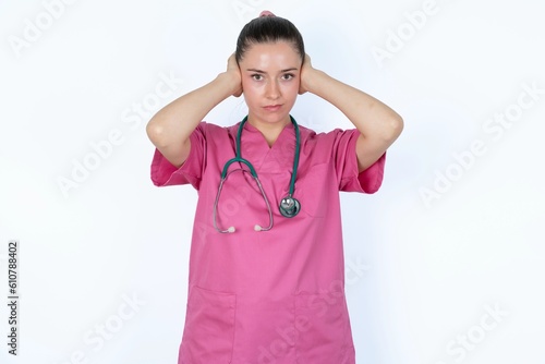 Frustrated young caucasian doctor woman wearing pink uniform over white background plugging ears with hands does not wanting to listen hard rock  noise or loud music.