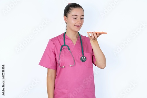 Εκτύπωση καμβά Smiling young caucasian doctor woman wearing pink uniform over white background sending voice message on her smart phone