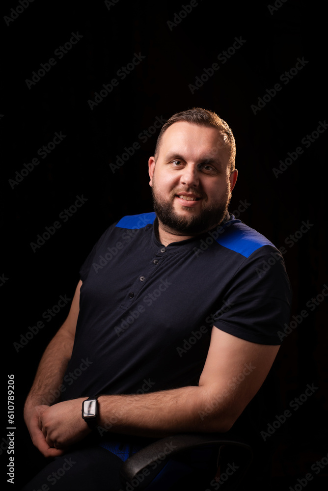 Portrait of a smiling young man with a beard. Dark background. Looks into the camera. Good-natured, contented, happy face. Portrait of a smiling young man with a beard. Dark background. Looks into the camera. Good-natured, contented, happy face.