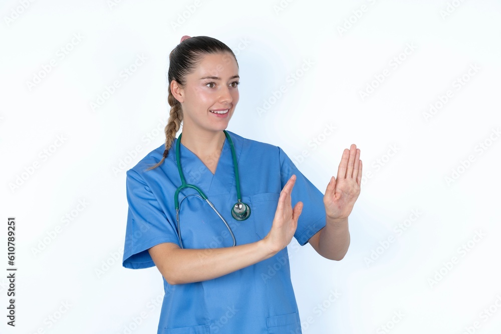 Displeased young caucasian doctor woman wearing medical uniform over white background keeps hands towards empty space and asks not come closer sees something unpleasant Displeased young caucasian doctor woman wearing medical uniform over white background keeps hands towards empty space and asks not come closer sees something unpleasant