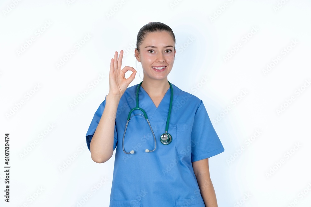 young caucasian doctor woman wearing medical uniform over white background hold hand arm okey symbol toothy approve advising novelty news young caucasian doctor woman wearing medical uniform over white background hold hand arm okey symbol toothy approve advising novelty news