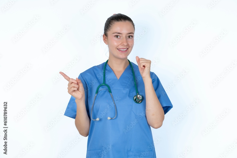 young caucasian doctor woman wearing medical uniform over white background points at empty space holding fist up, winner gesture. young caucasian doctor woman wearing medical uniform over white background points at empty space holding fist up, winner gesture.