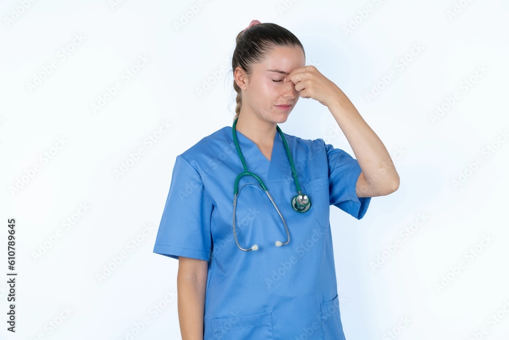 Sad young caucasian doctor woman wearing medical uniform over white background suffering from headache holding hand on her face Sad young caucasian doctor woman wearing medical uniform over white background suffering from headache holding hand on her face