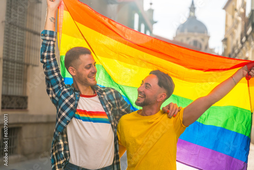 Portrait of gay male couple with rainbow flag at pride party in the city, lgbt concept