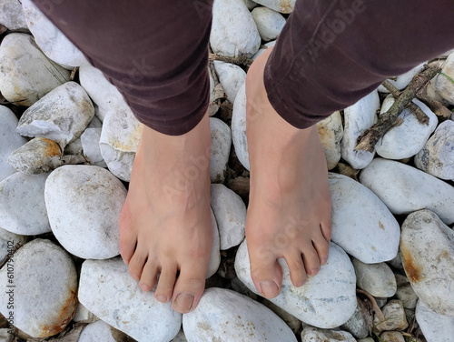 Girl's legs standing on large white stones. The feats are bear and the person is wearing brown trousers.