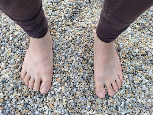 Girl's legs standing on small colorful stones. The feats are bear and the person is wearing brown trousers.