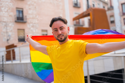 Portrait of attractive gay man smiling with rainbow lgbt flag in the city, pride and homosexual party